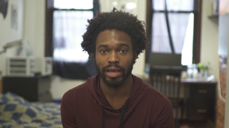 Yedoye Travis speaking to camera in his apartment